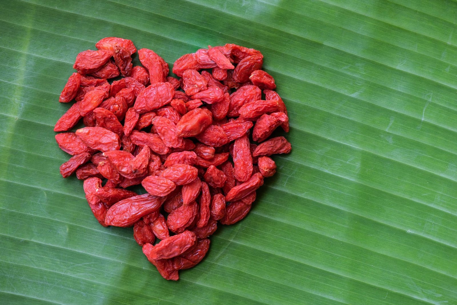 Goji berry fruits arranged in a heart shape on green banana back